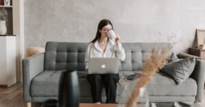 Woman sipping coffee while working on a laptop in a cozy home setting, highlighting remote work lifestyle.