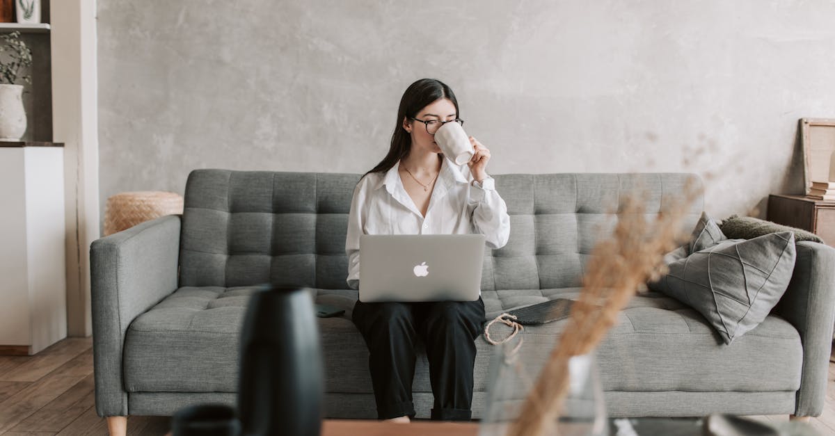 Woman sipping coffee while working on a laptop in a cozy home setting, highlighting remote work lifestyle.